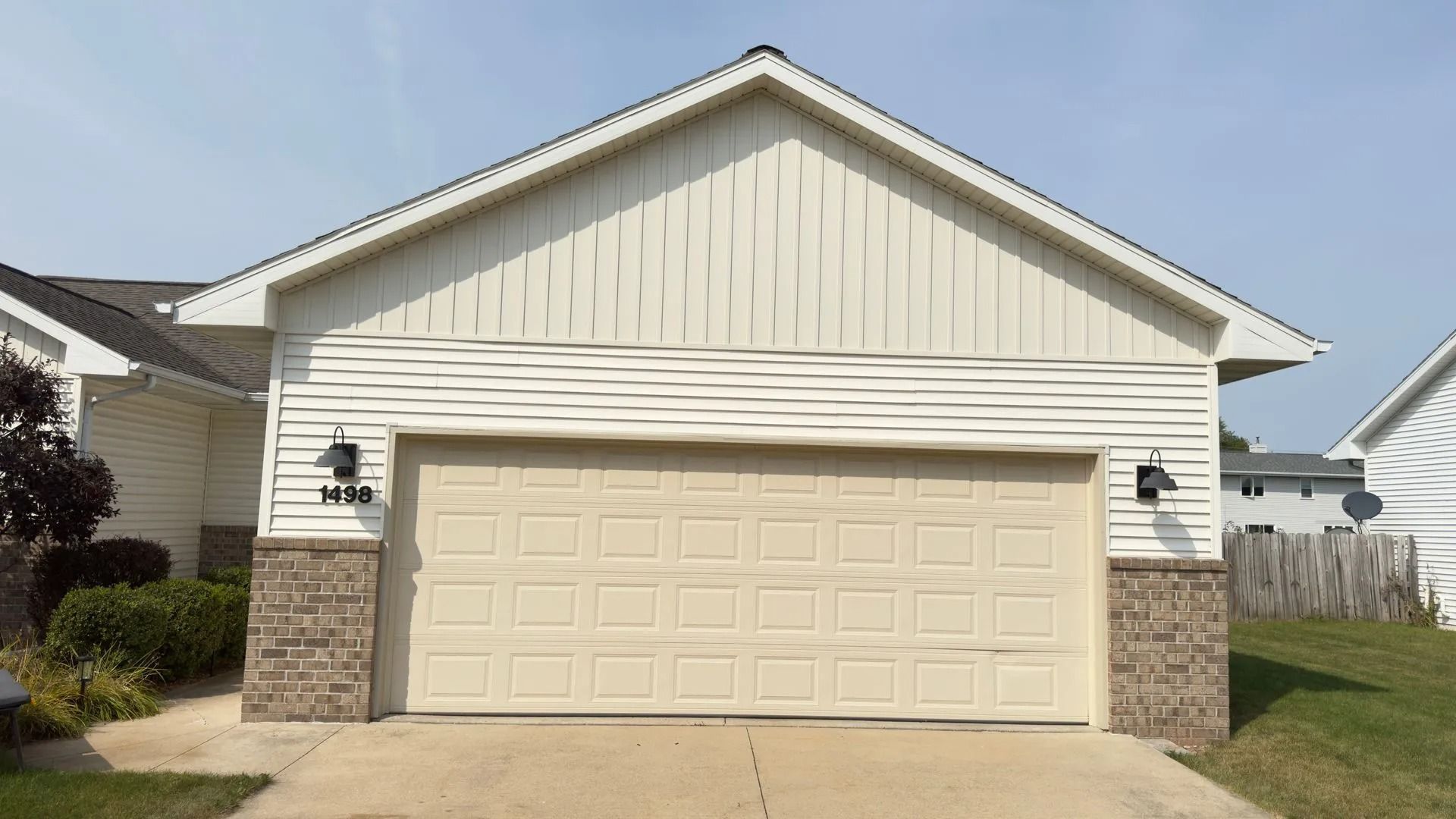 Beige garage door with tan siding and brown stone accents under a sunny sky.