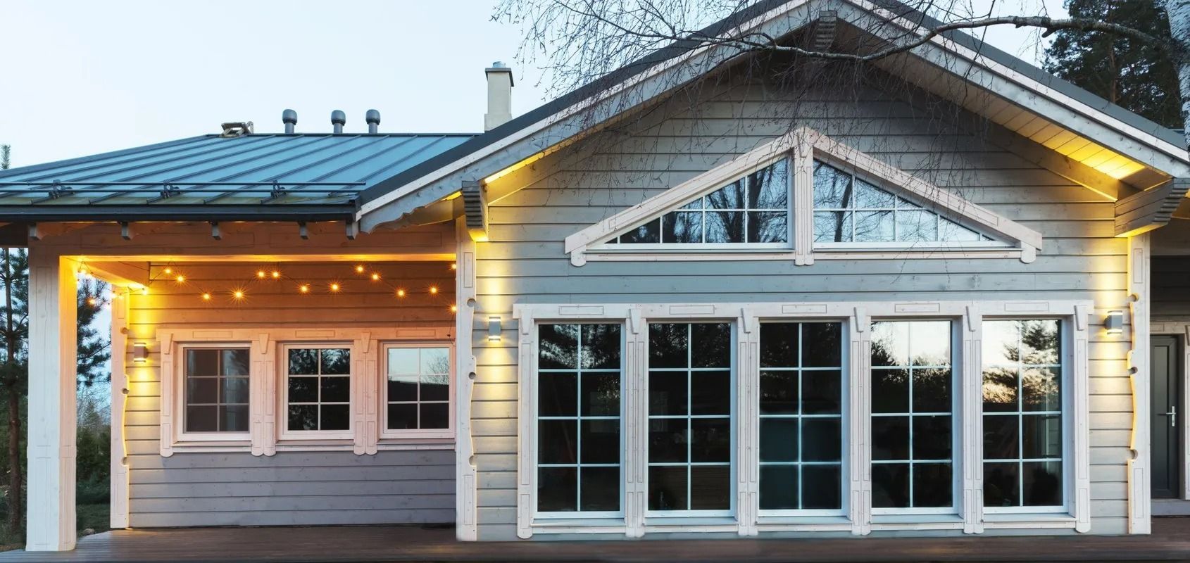 A light blue house with large windows and a covered porch, lit by string lights.