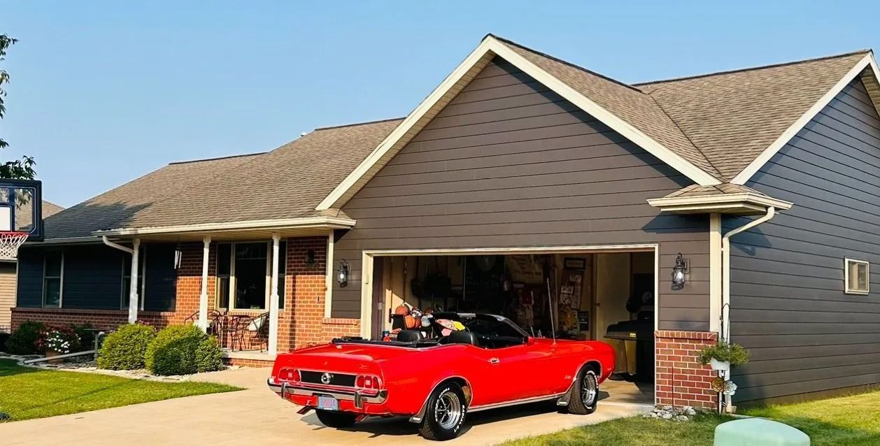 Red convertible parked in an open garage of a house with brown siding.