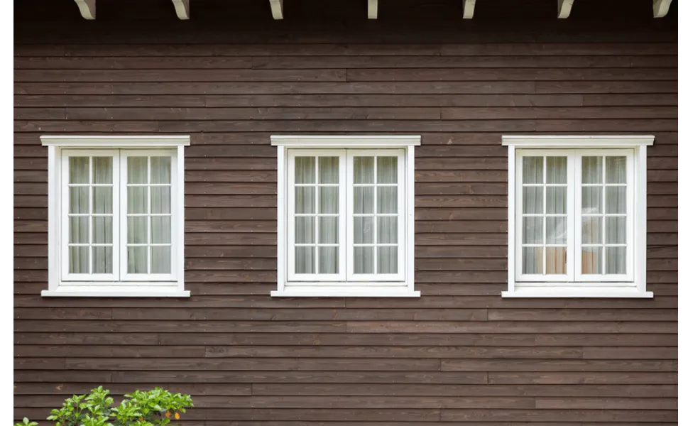 Three white-framed windows with vertical grids on a brown wooden exterior wall.