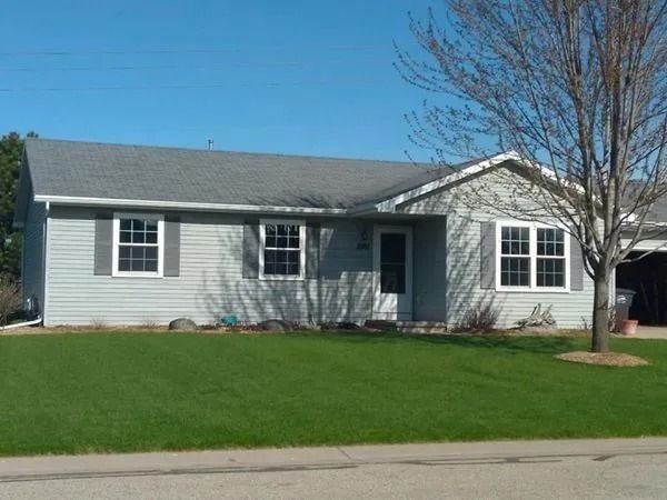 Gray house with gray roof, green lawn, tree in the yard.