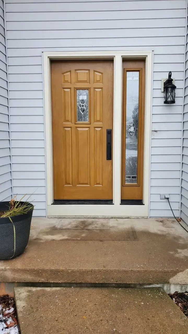 Brown front door with sidelight, light gray siding, and a small porch.