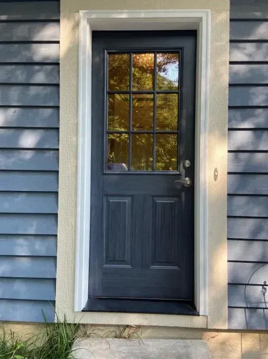 Dark blue door with glass pane in a white frame, set in blue siding.