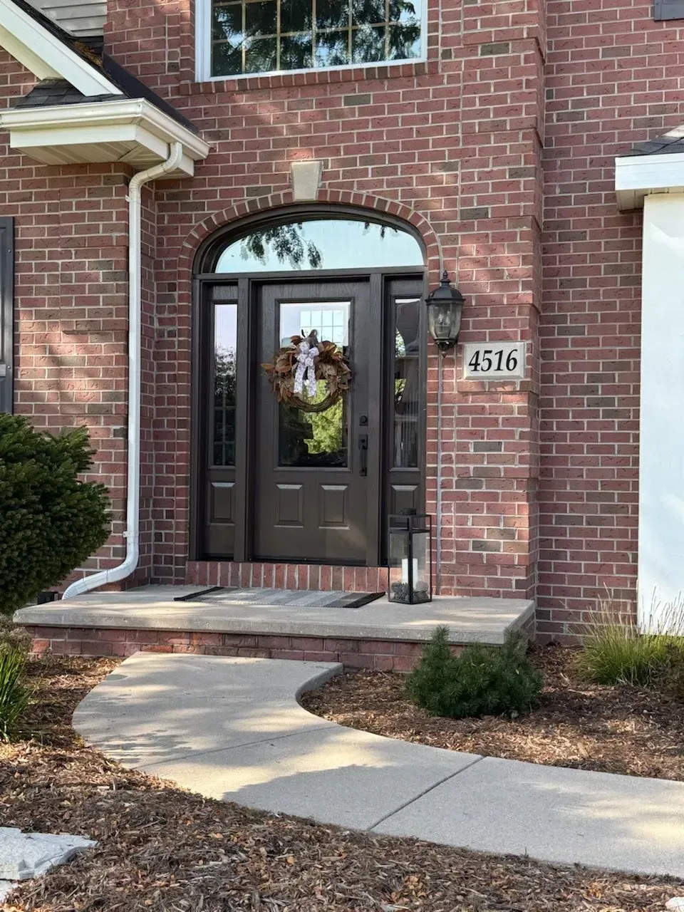 Brick house entrance with dark door, sidelights, arched window above. A wreath hangs on the door.