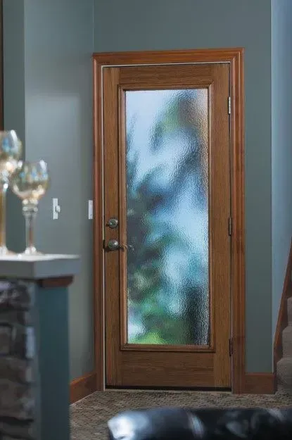 Wooden door with frosted glass panel, set in a wood frame, opens to a blurred outdoor scene.