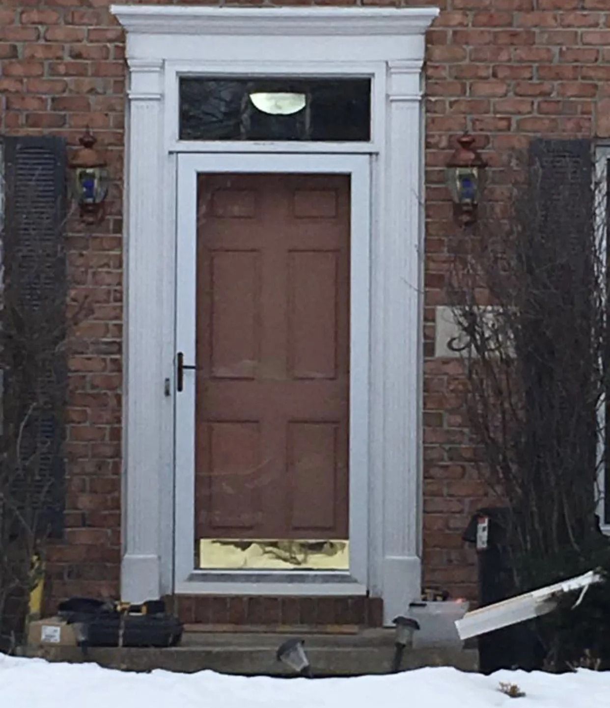 Brown front door with white trim, sidelights, and overhead transom, set in a red brick building.