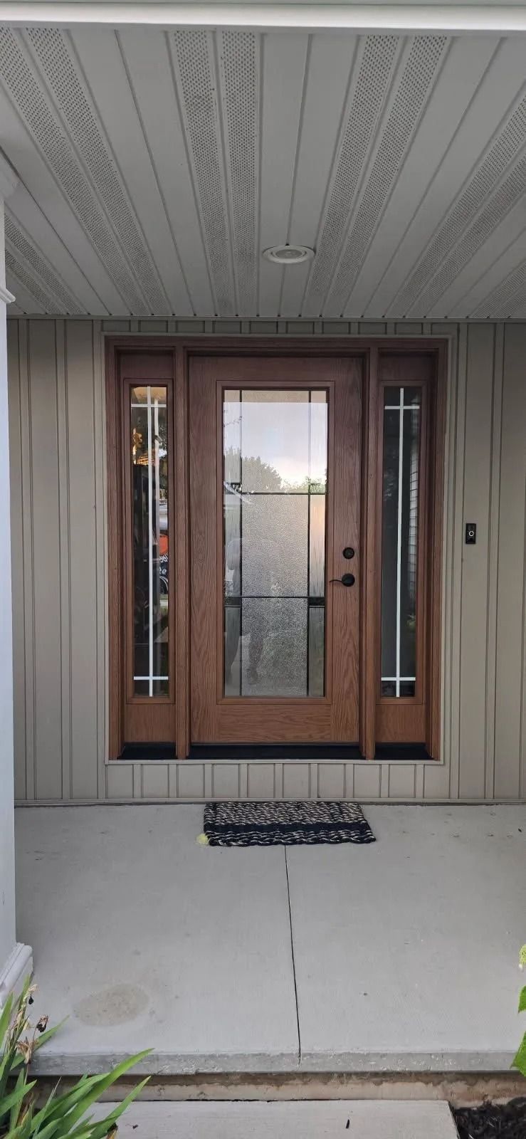 Exterior view of a front door with sidelights, featuring a brown wooden door with glass, and a concrete porch.