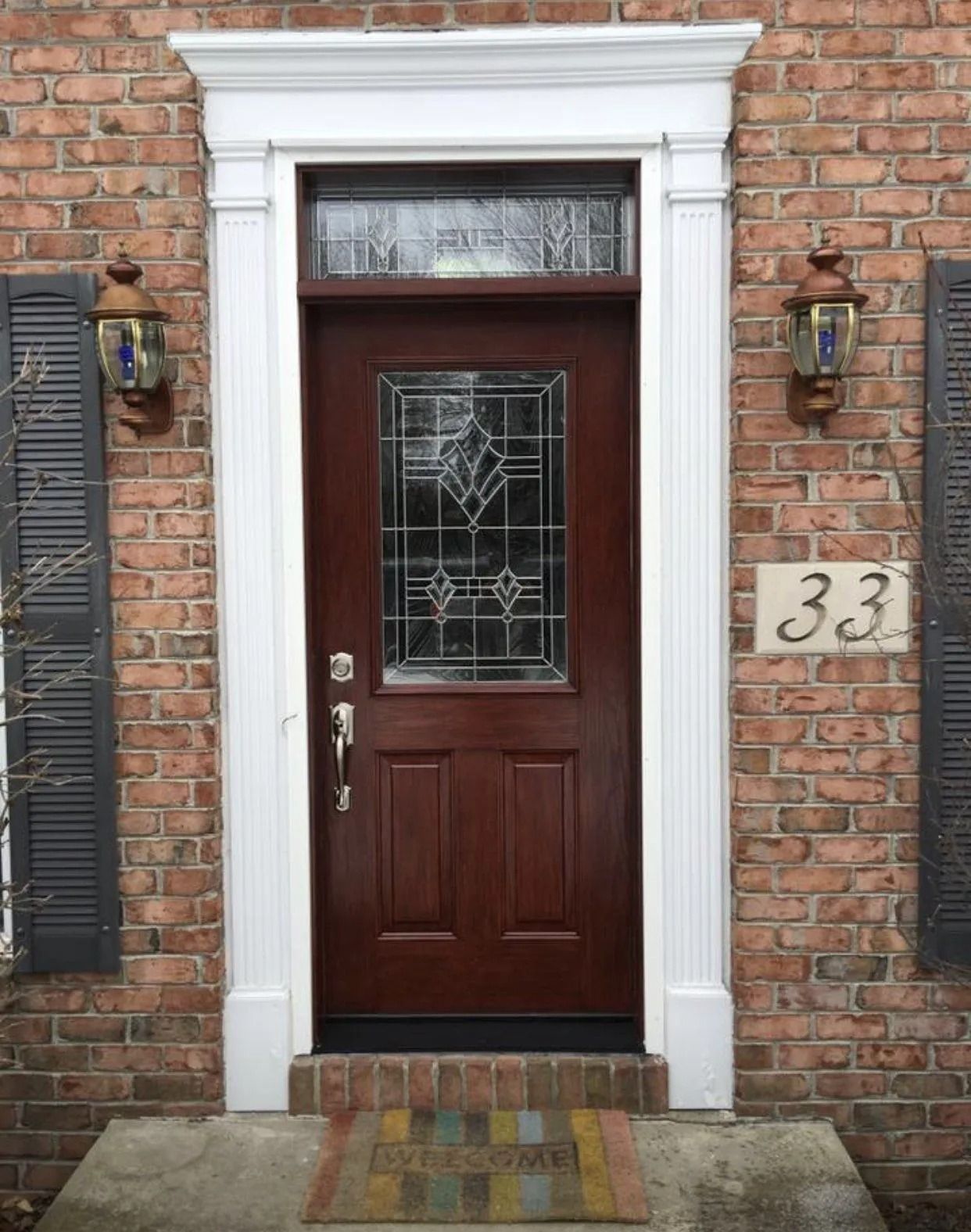 Brown door with leaded glass, white trim, brick facade, and address 33.