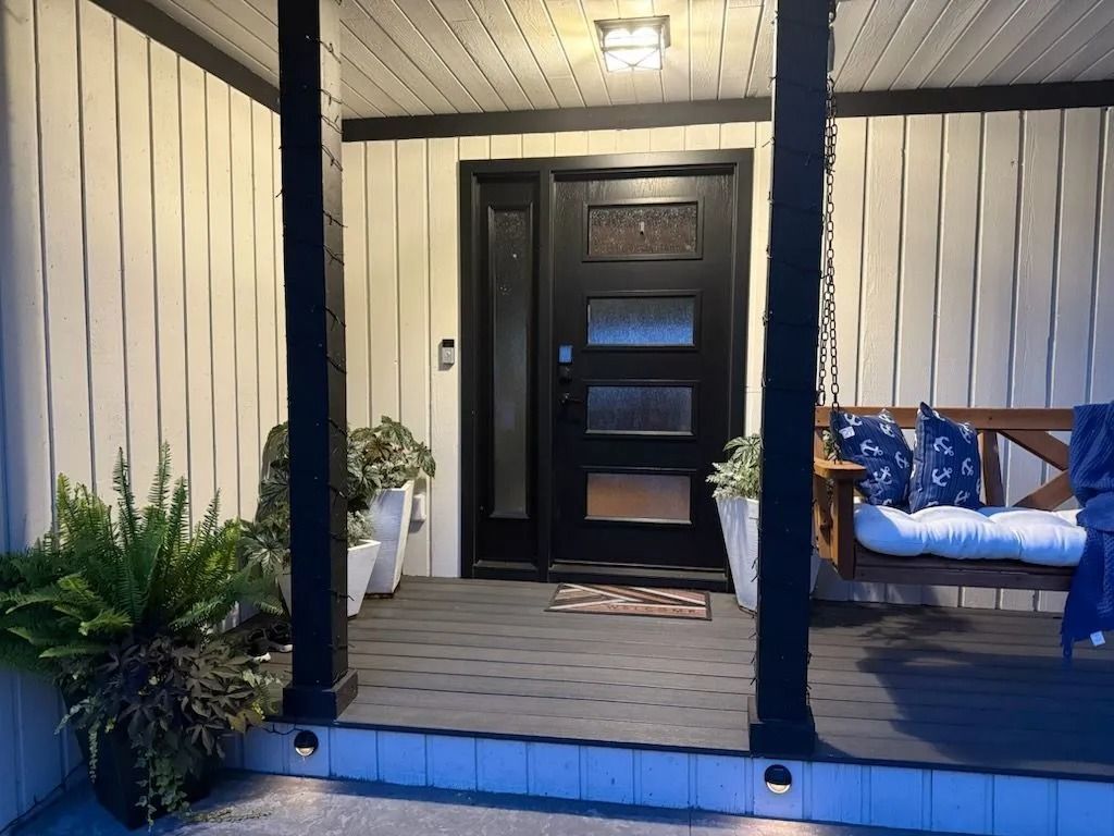 Black front door with sidelight and porch swing. Black and white exterior with potted plants.