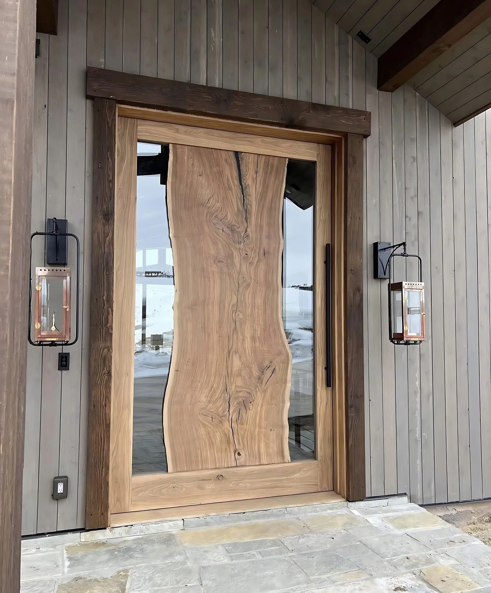 Wooden door with glass panel, rustic style, flanked by lanterns and set in a wooden frame.