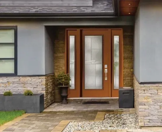 Brown front door with sidelights, set in a stone and stucco facade, leading to a home.