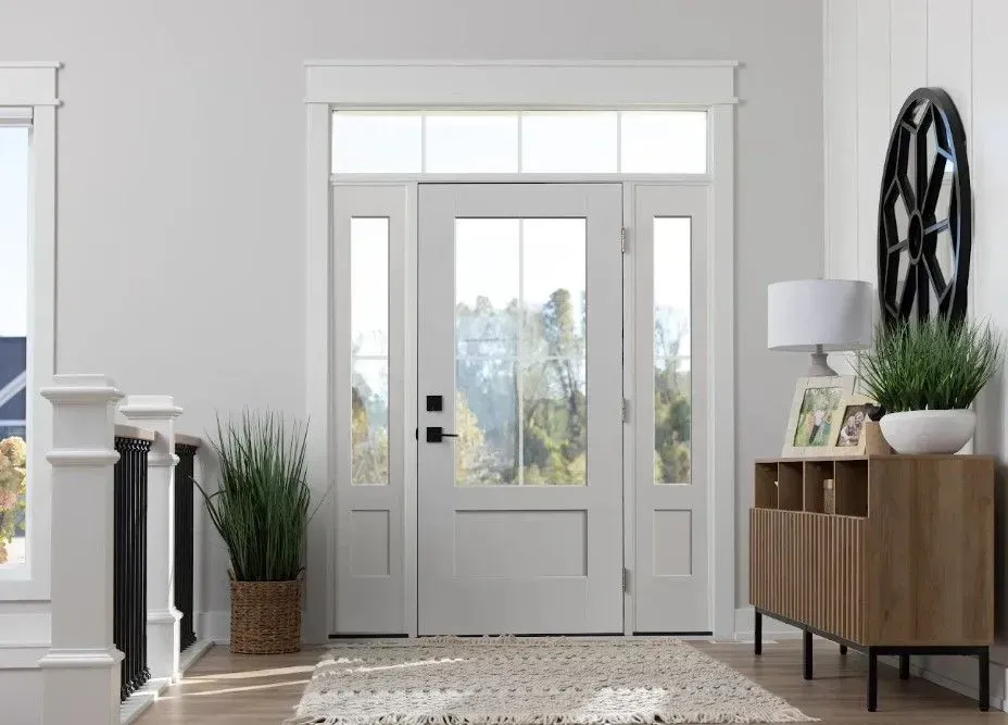 Bright entryway with white door, sidelights, and transom. Features a wood console, rug, and greenery.