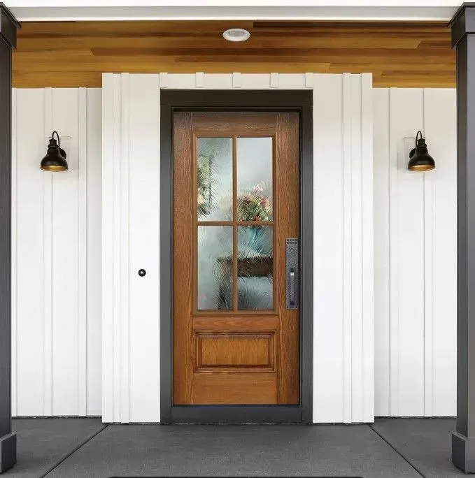 Brown wooden front door with glass panels, flanked by white siding, black sconces, and porch columns.