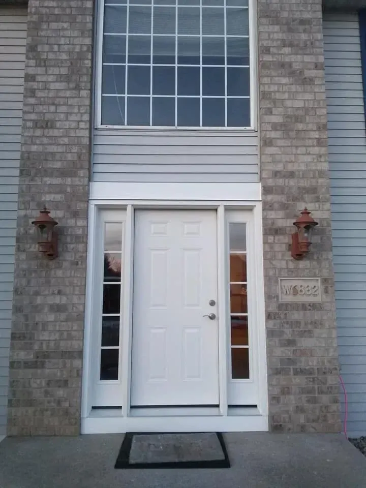 White front door with sidelights, brick columns, large window above, sconces, and address plaque.