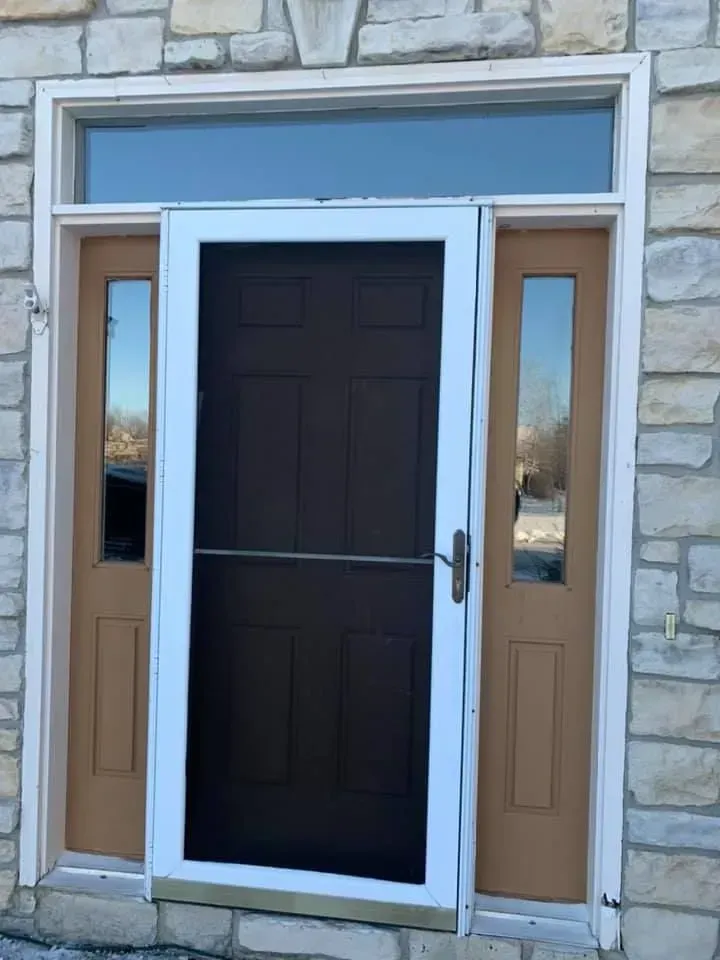 Screen door on a brown front door with sidelights; set in a stone wall.
