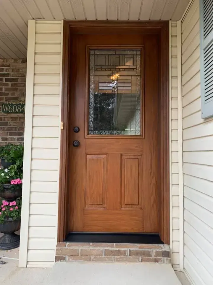 Brown wooden front door with glass pane, set in a cream-colored frame and siding.