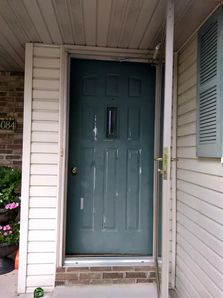 Dark teal door with peeling paint, open screen door, brick threshold, and light-colored siding.