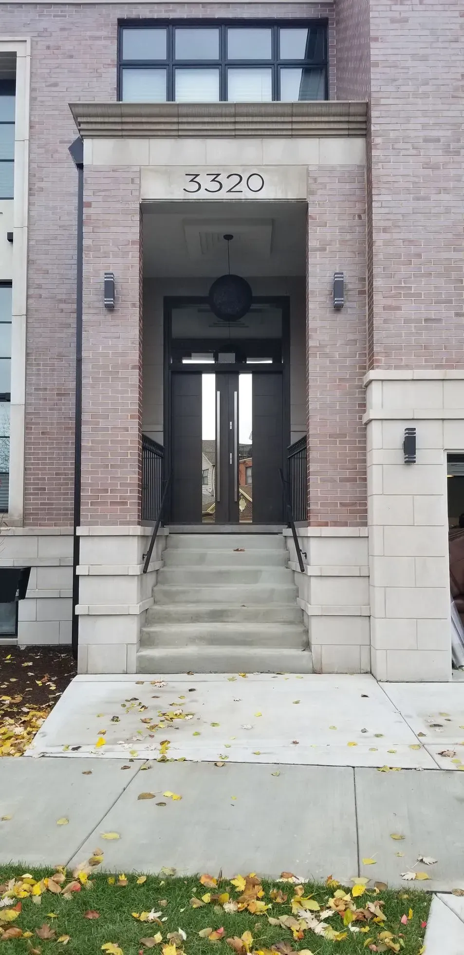 Building entrance with address 3320 above double doors and steps, brick facade, sidewalk, and grass.