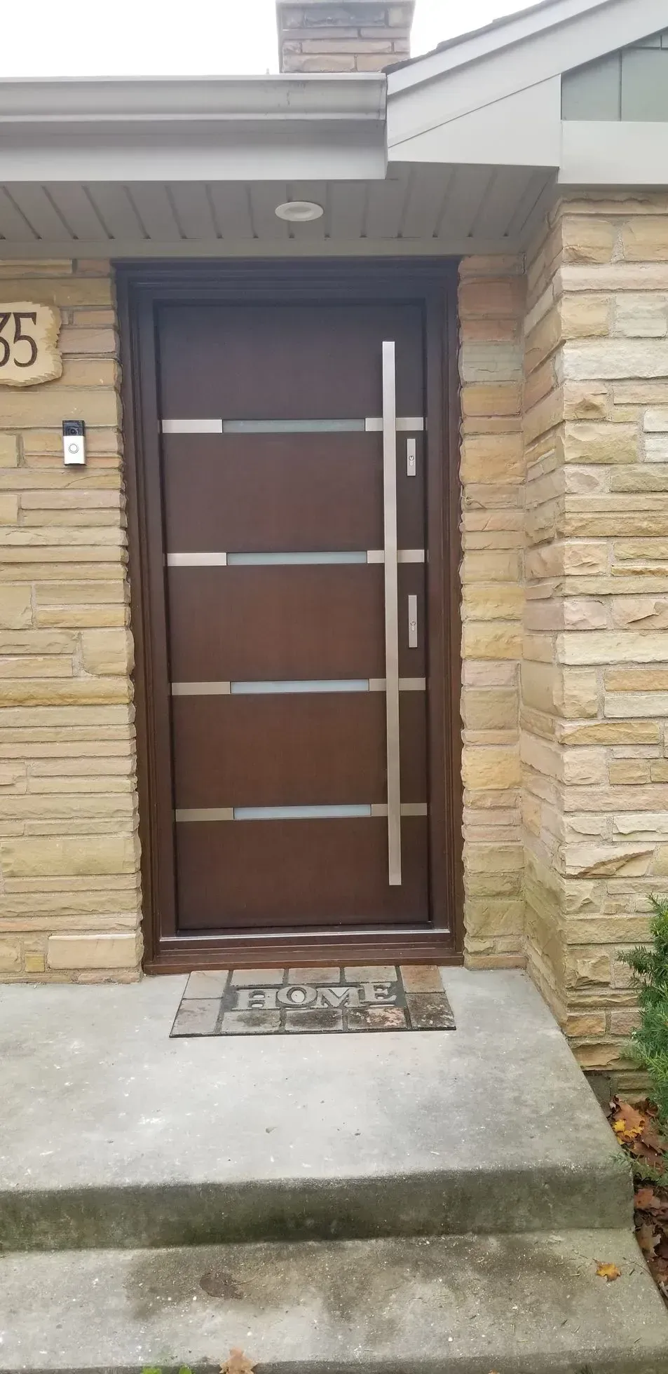 Brown door with horizontal silver stripes and vertical handle, set in a stone facade.