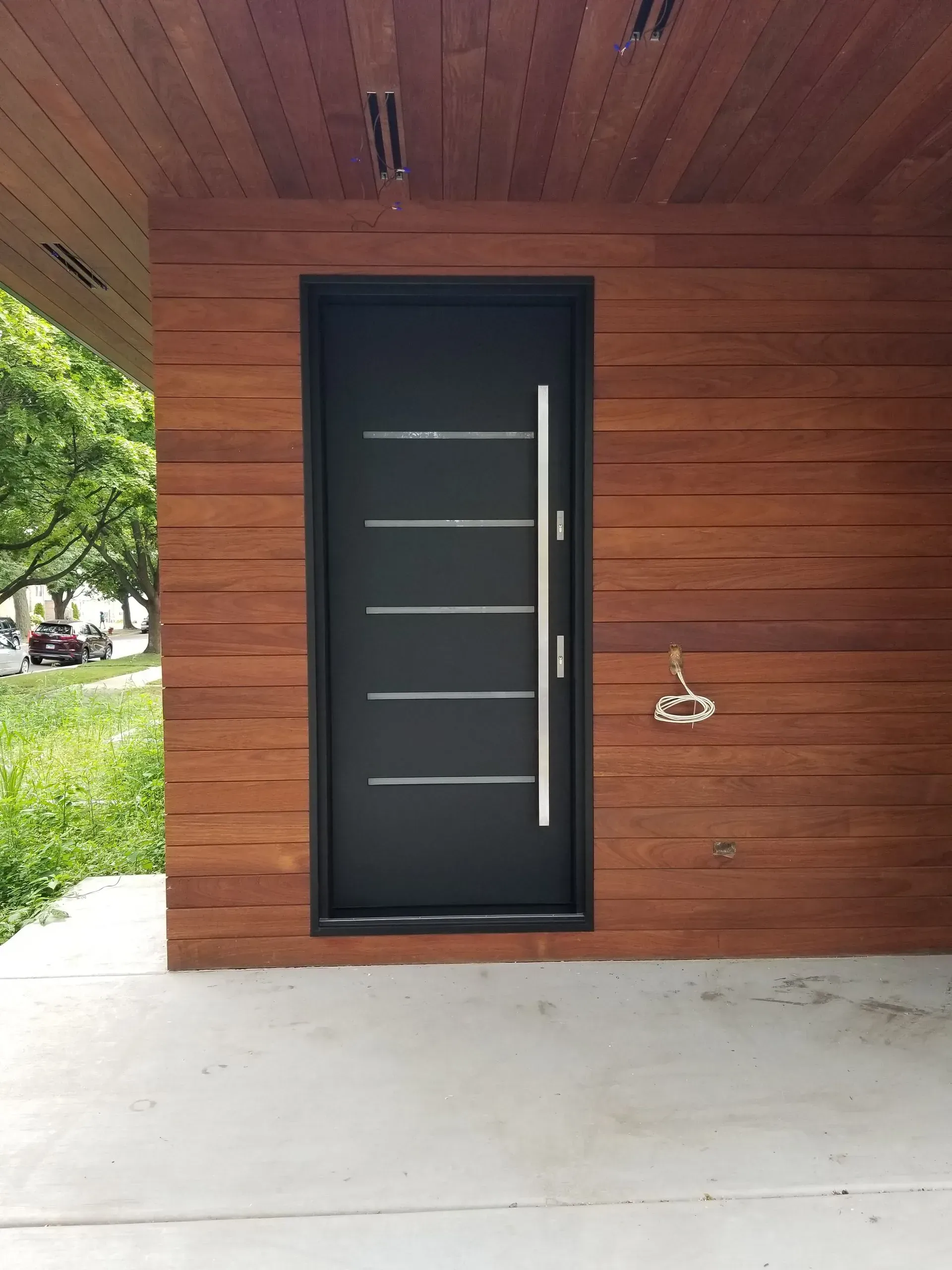 Black modern door with horizontal silver stripes and long handle, set in a wood panel exterior.