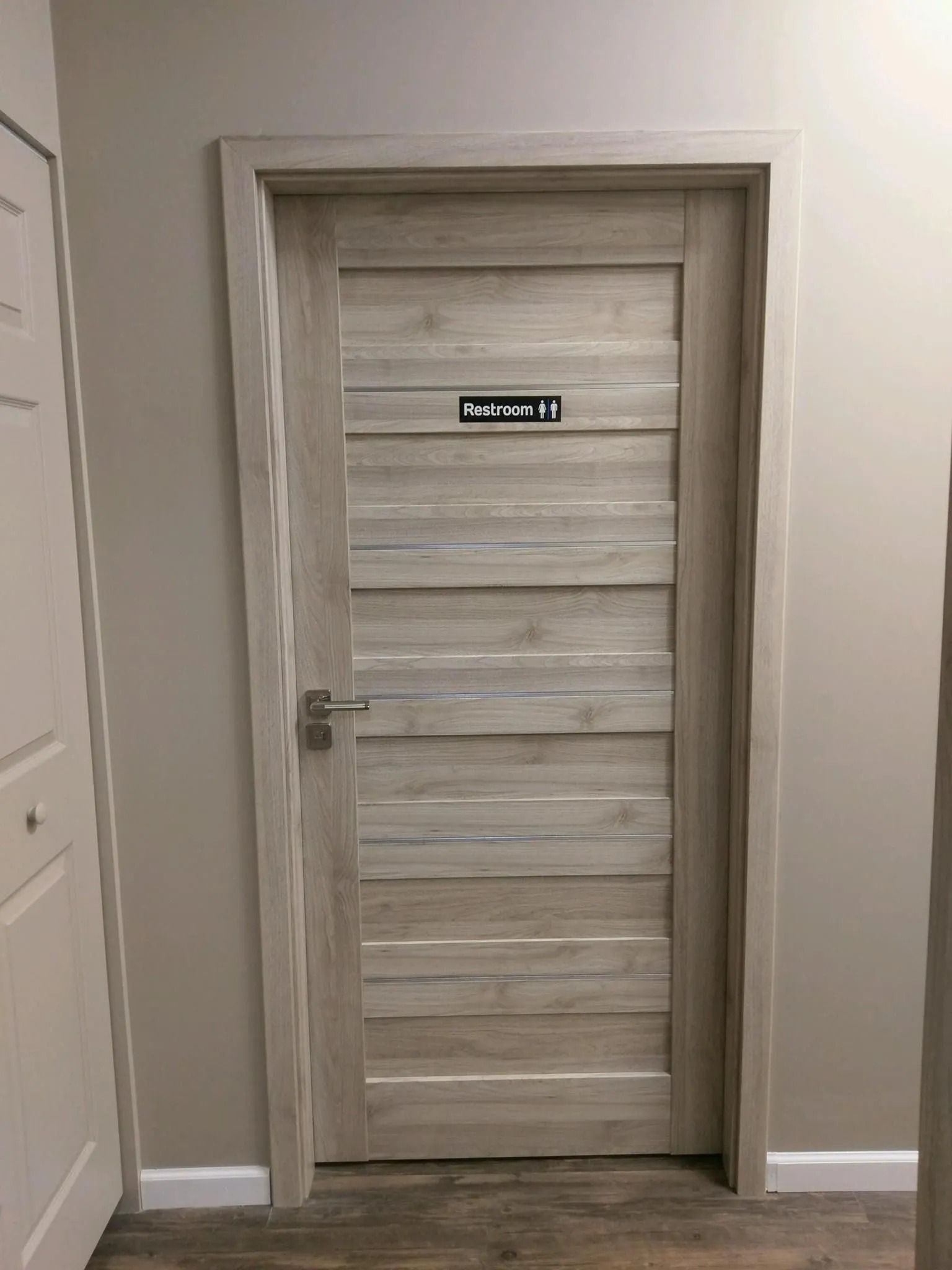 A light-colored wooden door with a rectangular sign in Arabic above the handle.