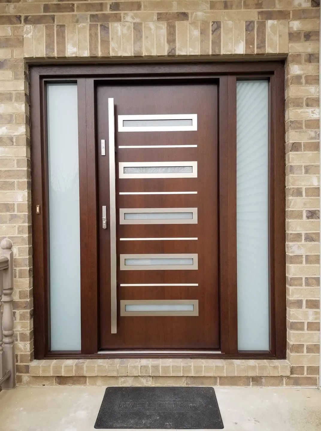 Brown modern front door with sidelights, brick exterior.