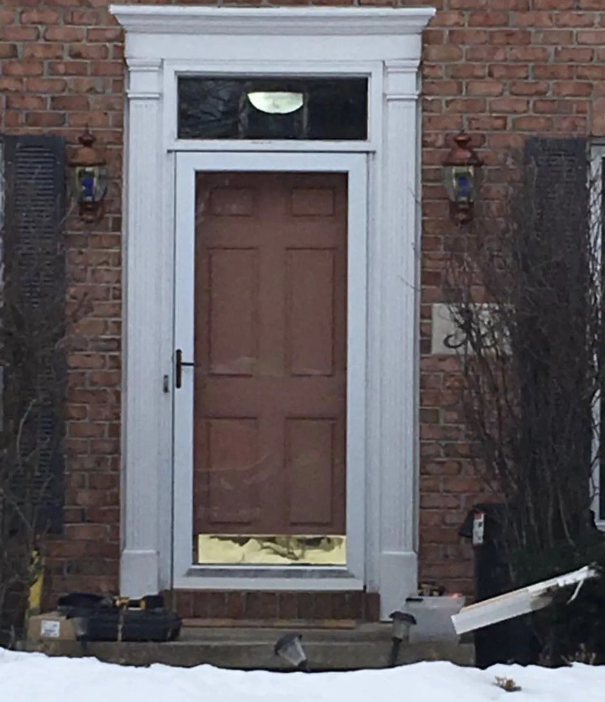 Brown door in white frame with gold kick plate on brick building with snow.