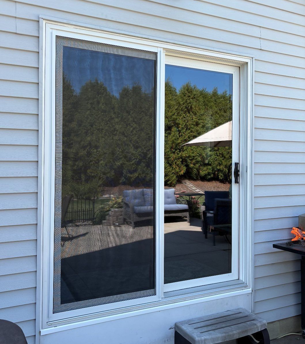 Sliding glass door with a screen, reflecting a patio with furniture and trees.