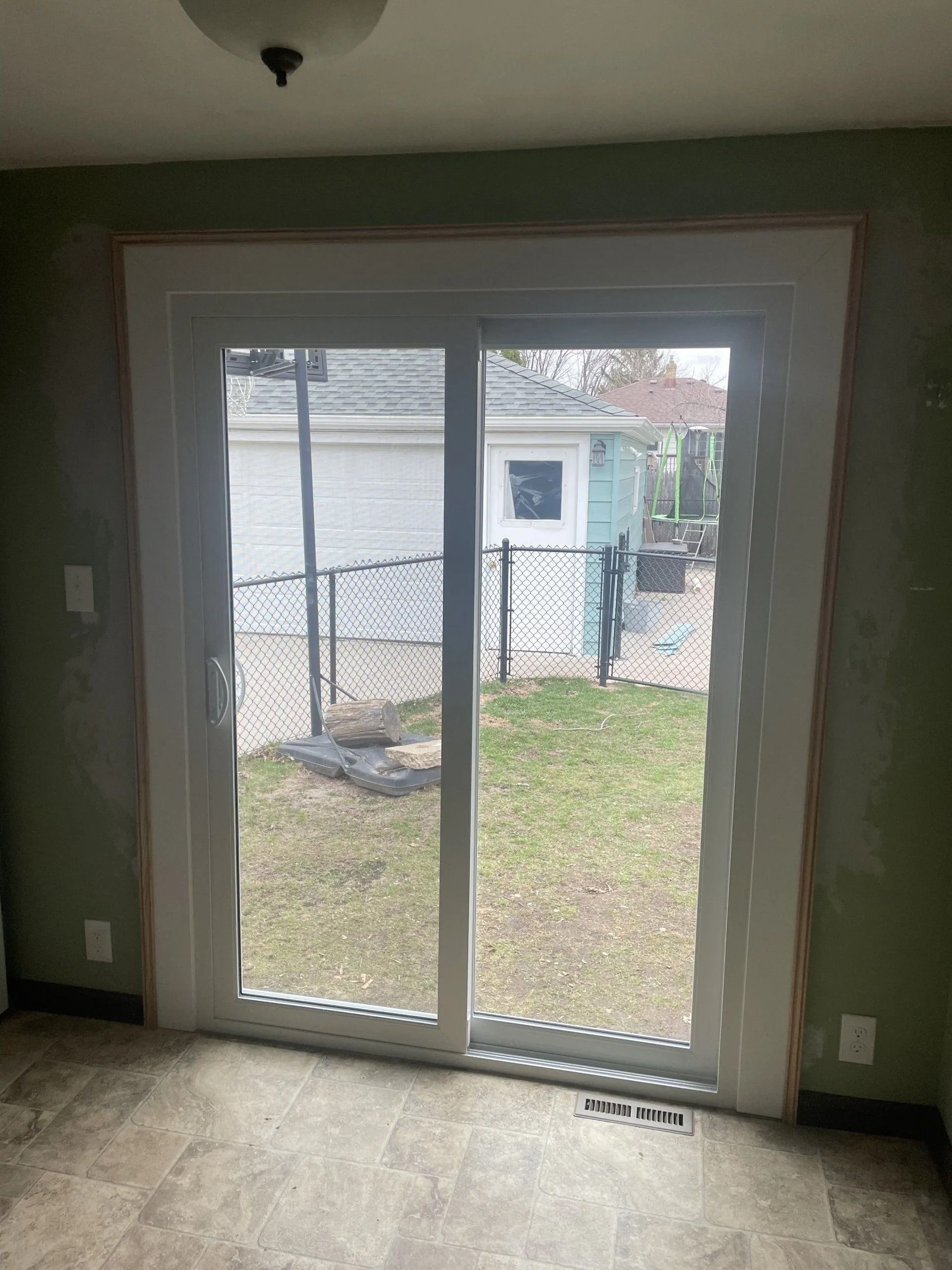 Two-pane sliding glass door with white frame, looking out to a backyard with chain-link fence and green grass.