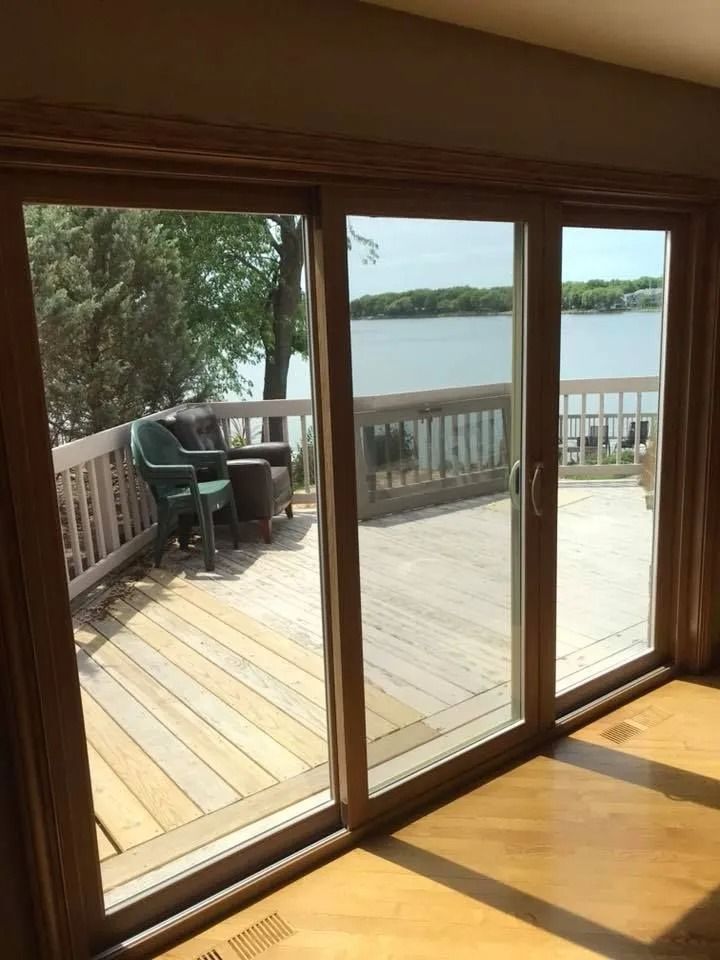 Sliding glass doors open to a wooden deck overlooking a lake, with chairs and railing visible.