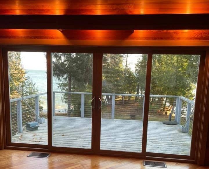 Sliding glass doors open onto a wooden deck overlooking a lake and trees.