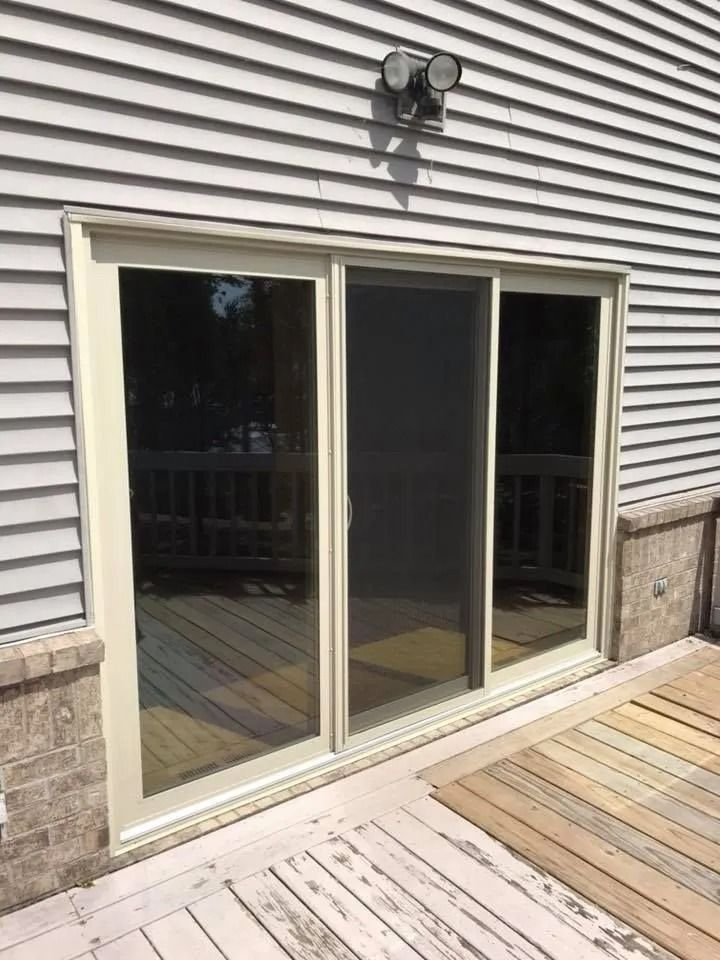 Sliding glass door with screen on a house's exterior, leading to a wooden deck.