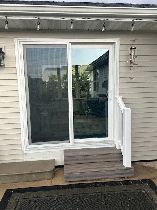 Sliding glass door with steps, surrounded by siding. A screened door is on the left.