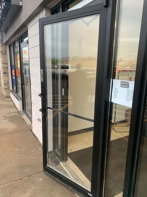 A glass door is open, revealing the inside of a business, next to a concrete walkway.
