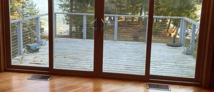 Sliding glass doors open onto a wooden deck overlooking trees and water. Inside is a wood floor.