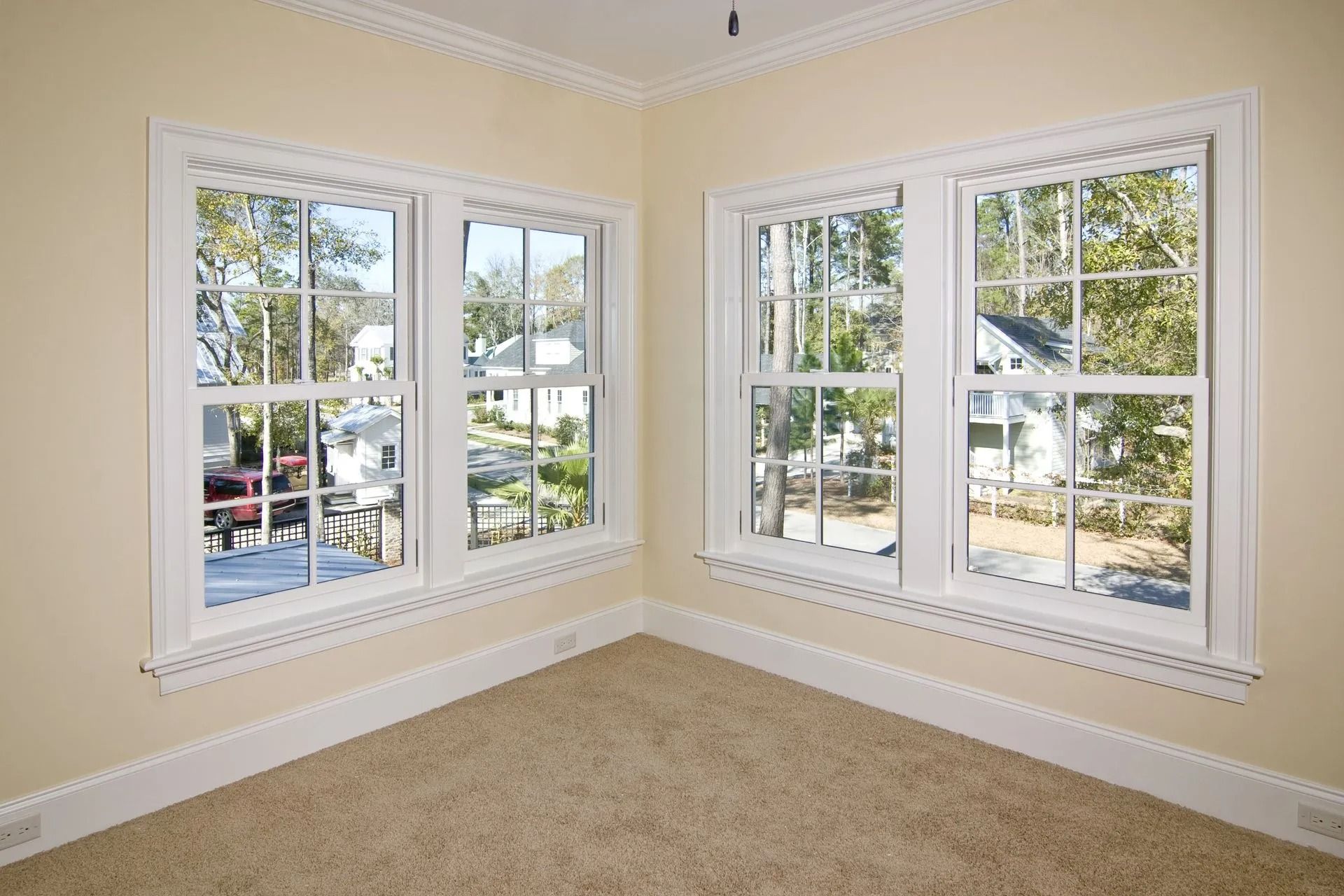 Corner room with two white-framed windows, beige walls, crown molding, and a light brown carpet.