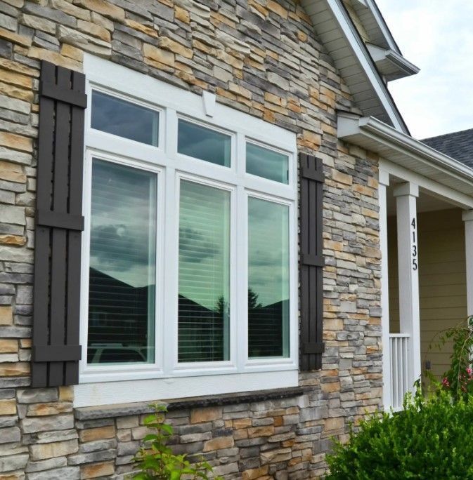 Stone house exterior with white-framed window, dark shutters, and a portion of a covered porch.