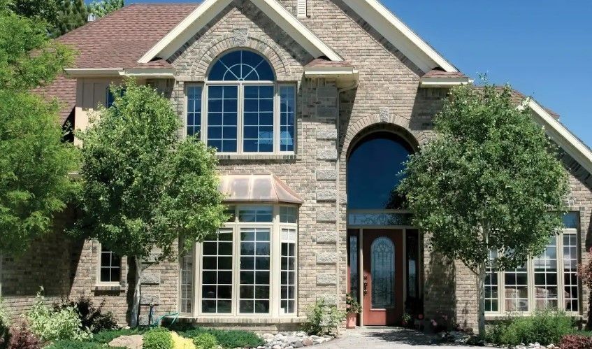 Brick facade home with multiple windows, arched entry, and trees.