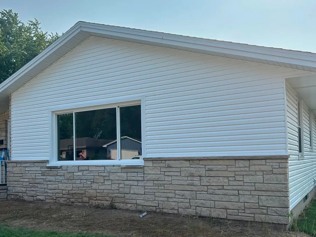 White-sided house with a large window and stone-like veneer on the lower part of the exterior.