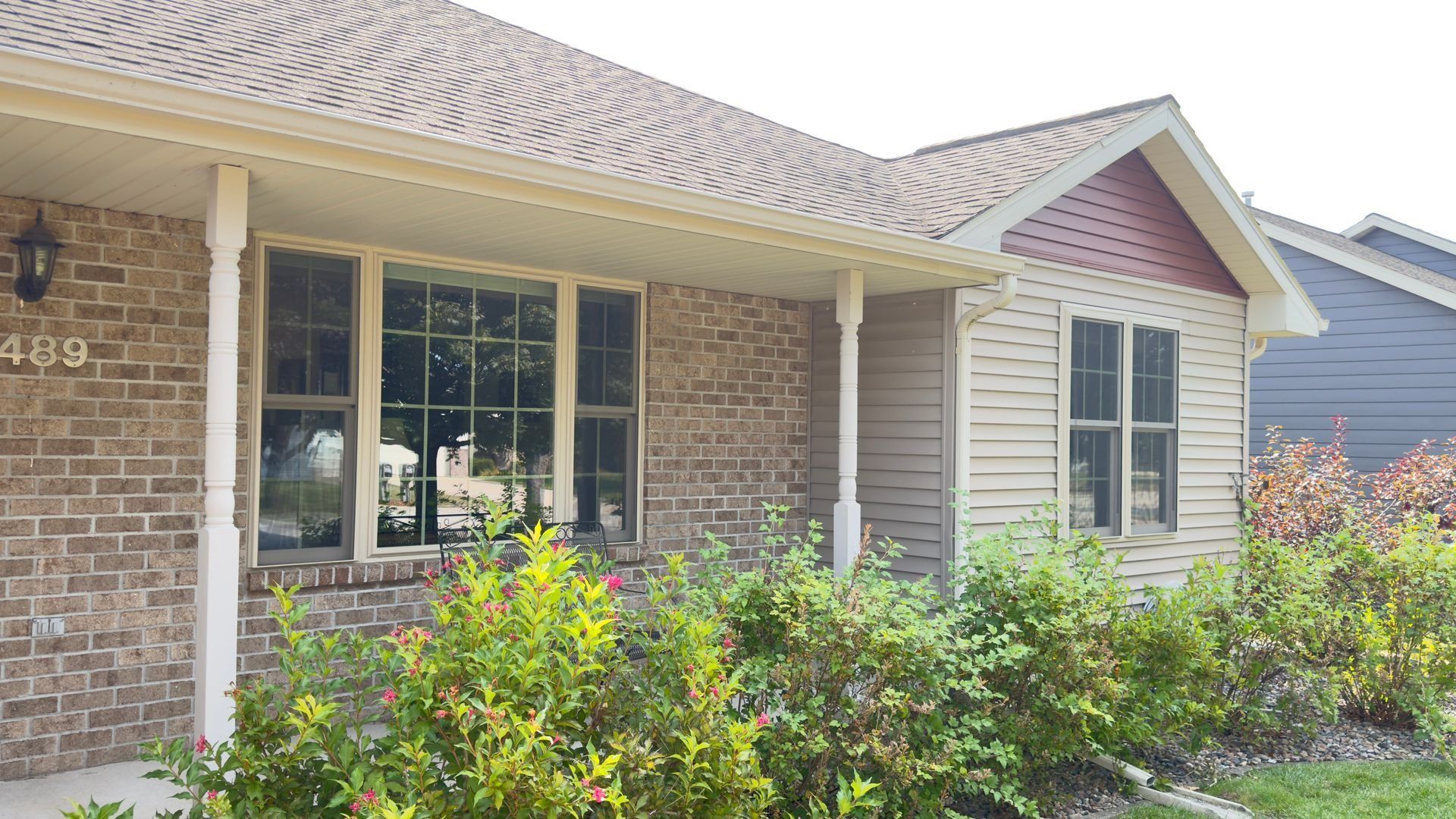 Tan and brick house with bushes in front.
