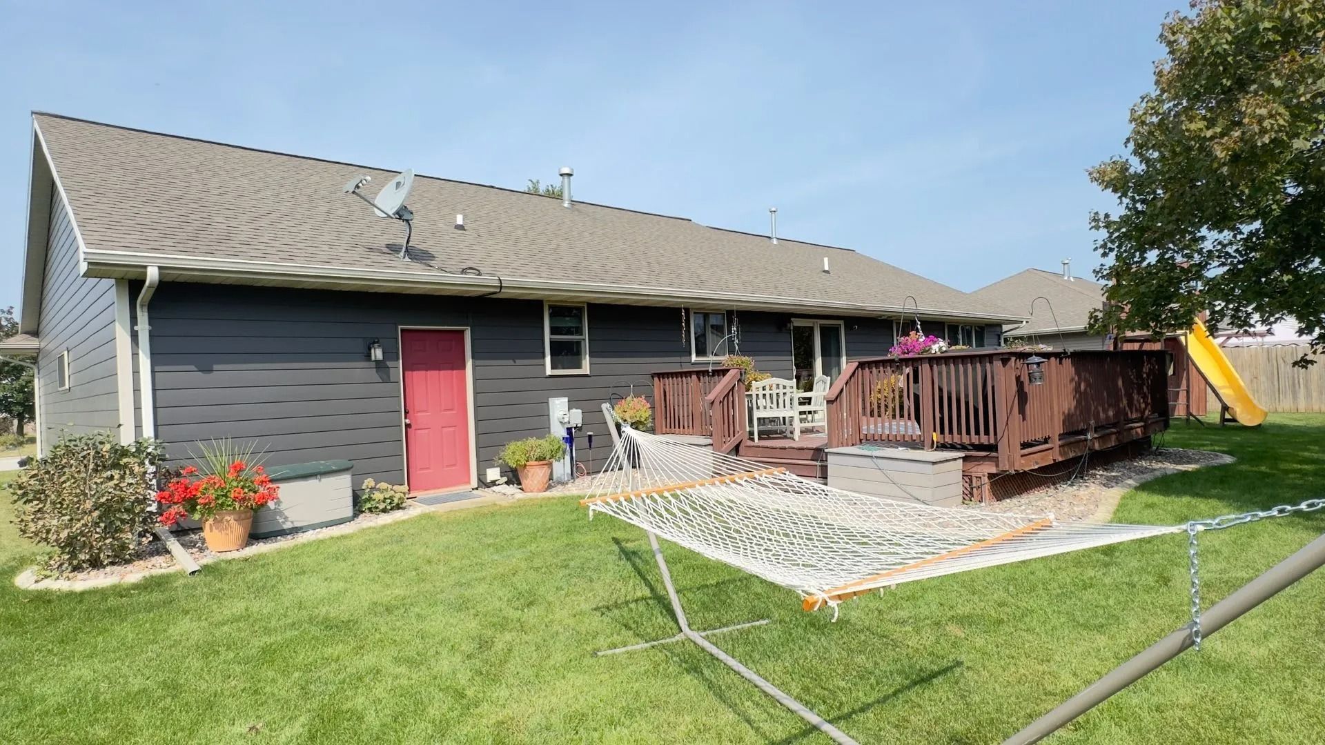 Backyard with dark siding, red door, wooden deck, hammock, and a yellow slide.