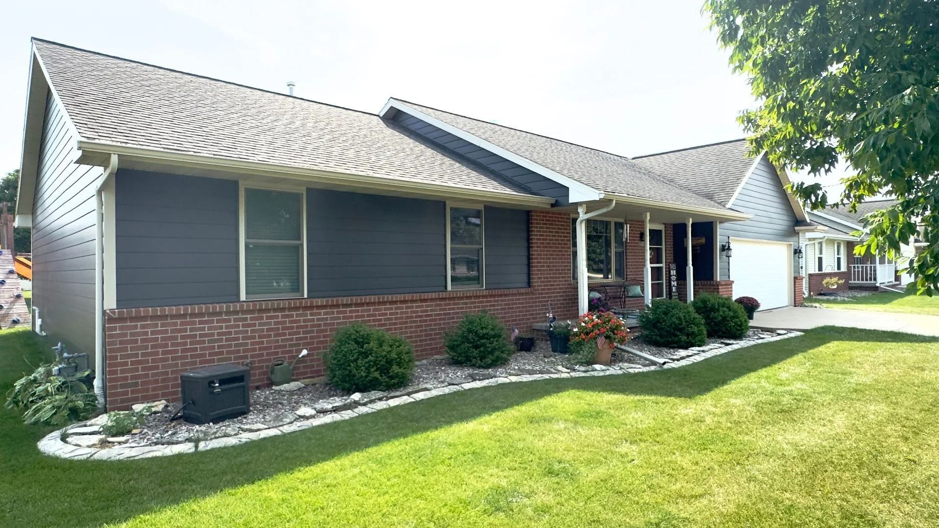 Low-angle view of a one-story brick home with dark siding, a well-kept lawn, and landscaping.