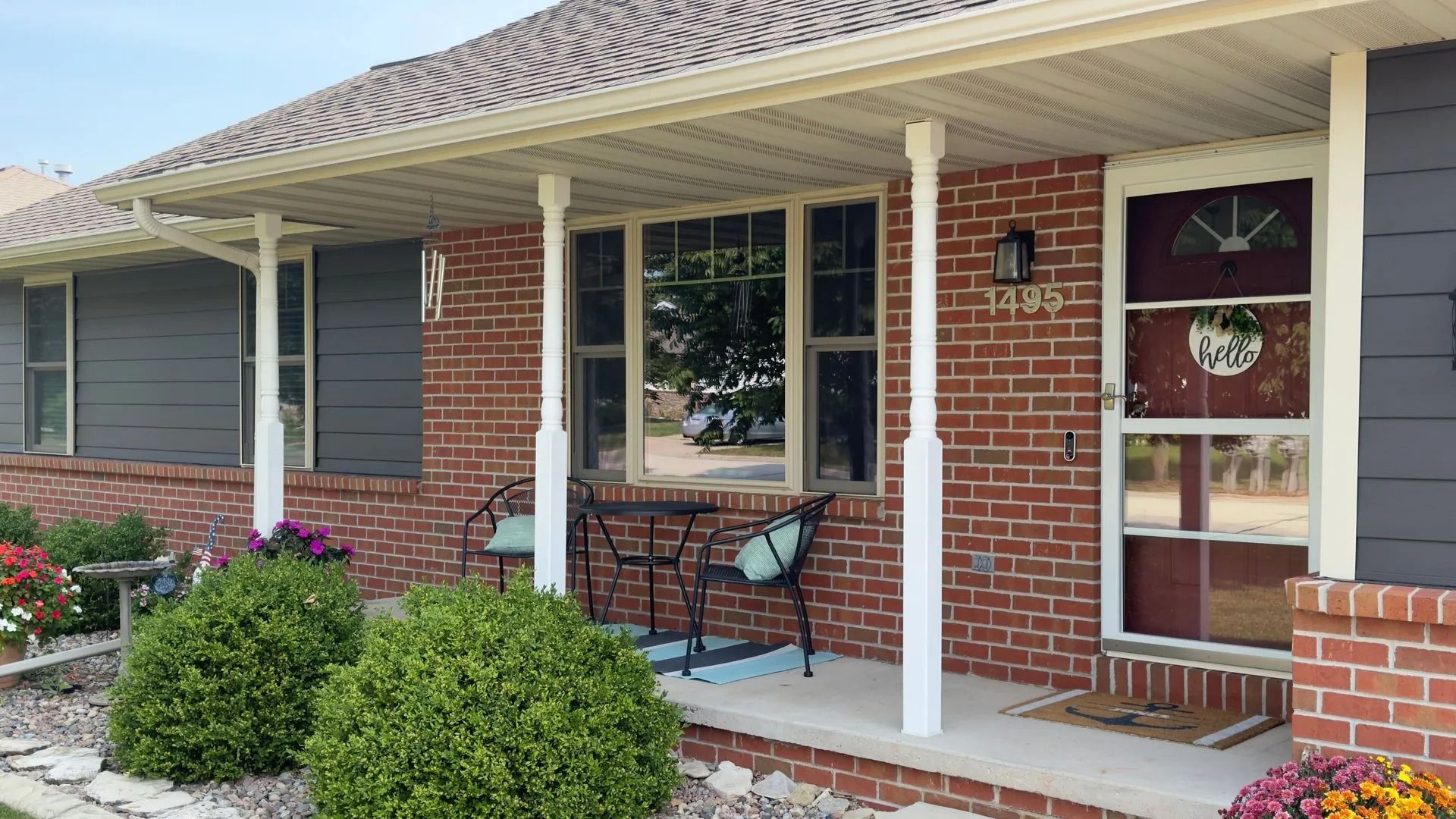 Red brick house with a covered porch. White columns, grey shutters, and a small sitting area.
