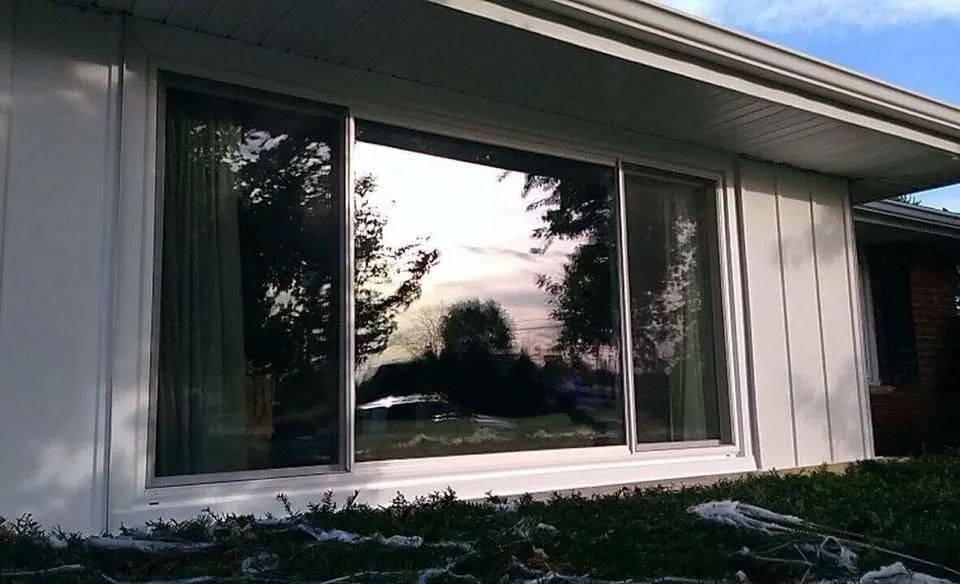 Large sliding glass window reflecting trees and sky in a white building.