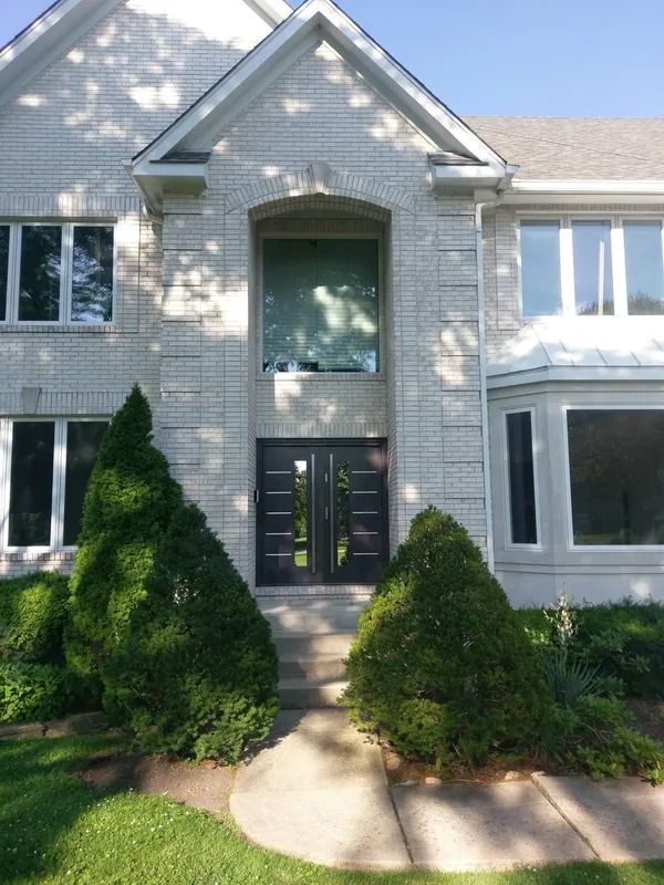 Stone-faced house with double black doors, tall windows, and two cone-shaped green bushes framing the entrance.