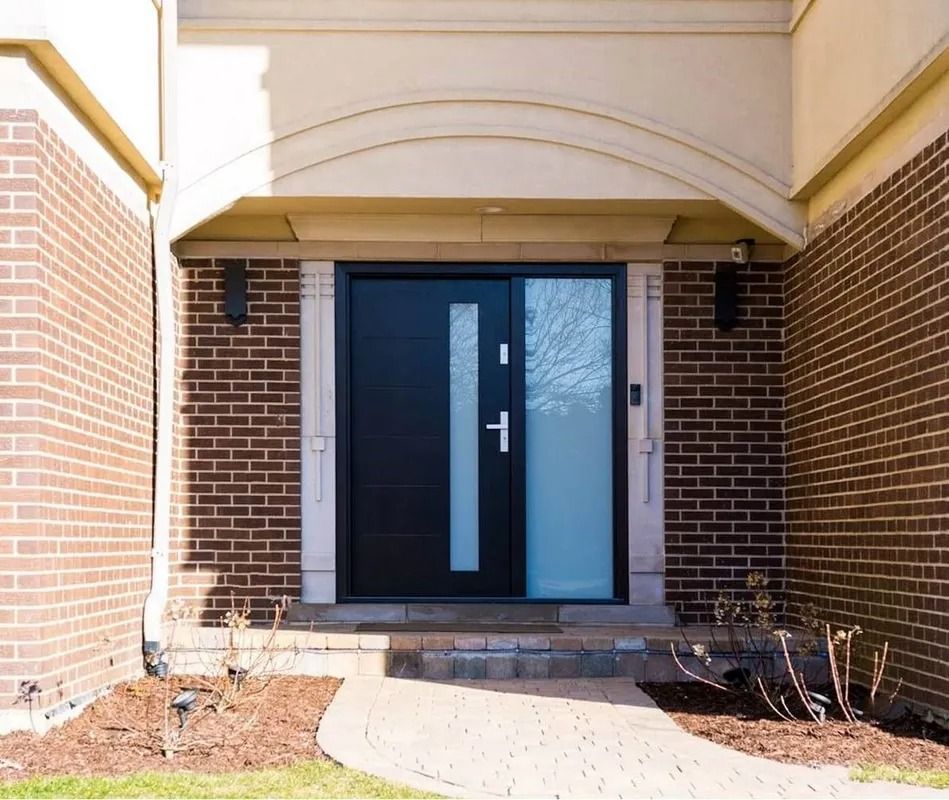 Black front door with sidelight, flanked by brick walls, leading to a home, under an arched entryway.