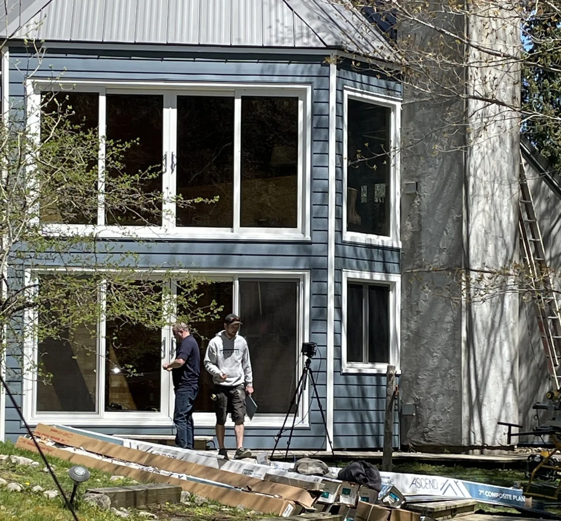 Two people stand near a blue house with large windows, possibly under construction.