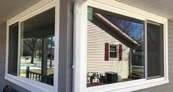 Corner windows on a house reflect the yard and neighboring house. White trim.