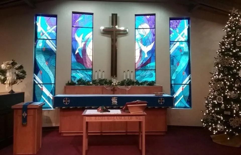 Church altar with stained glass, cross, candles, and Christmas tree.