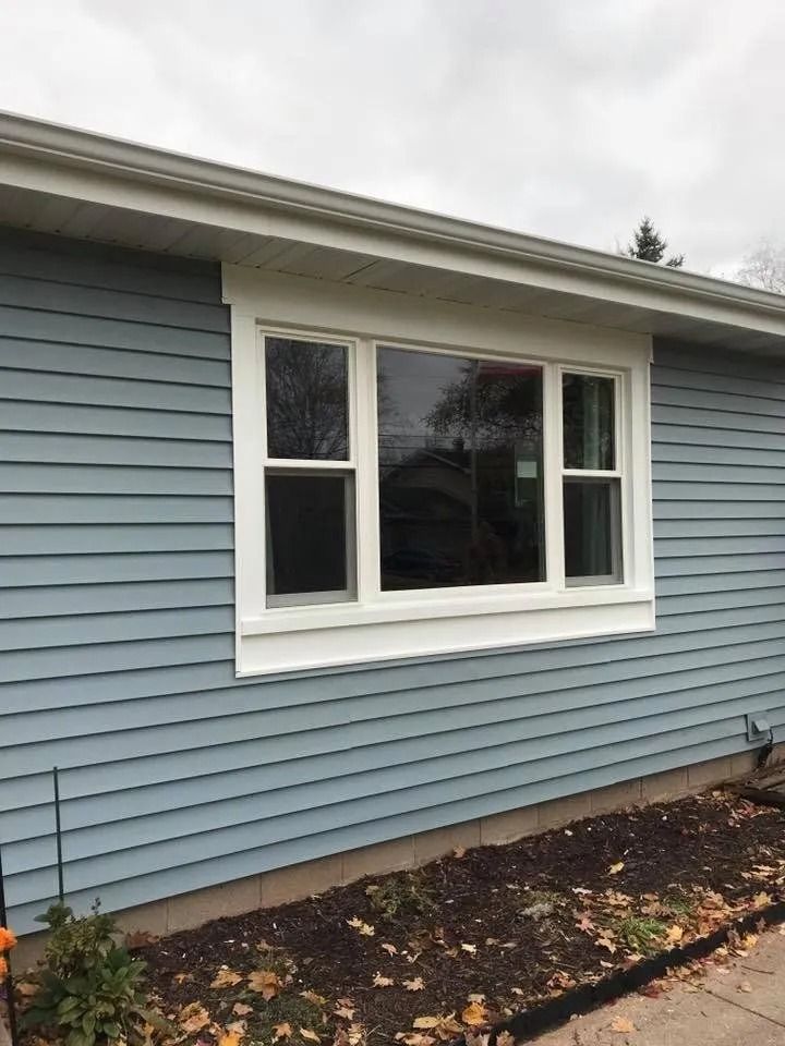 Blue siding with a white-framed window. Brown mulch and landscaping sit below the wall.